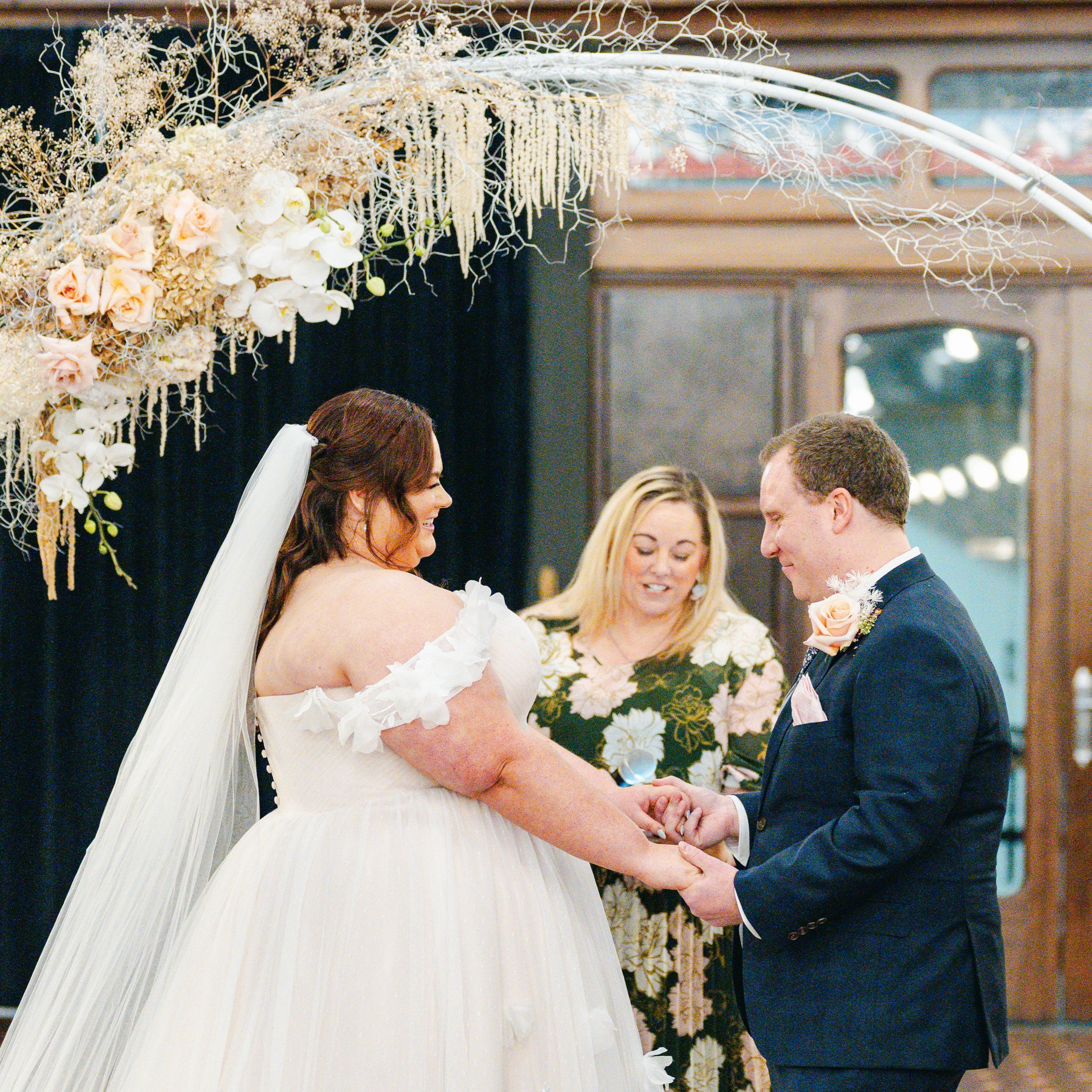 Wedding ceremony with a couple under an arch decorated with flowers, surrounded by guests.